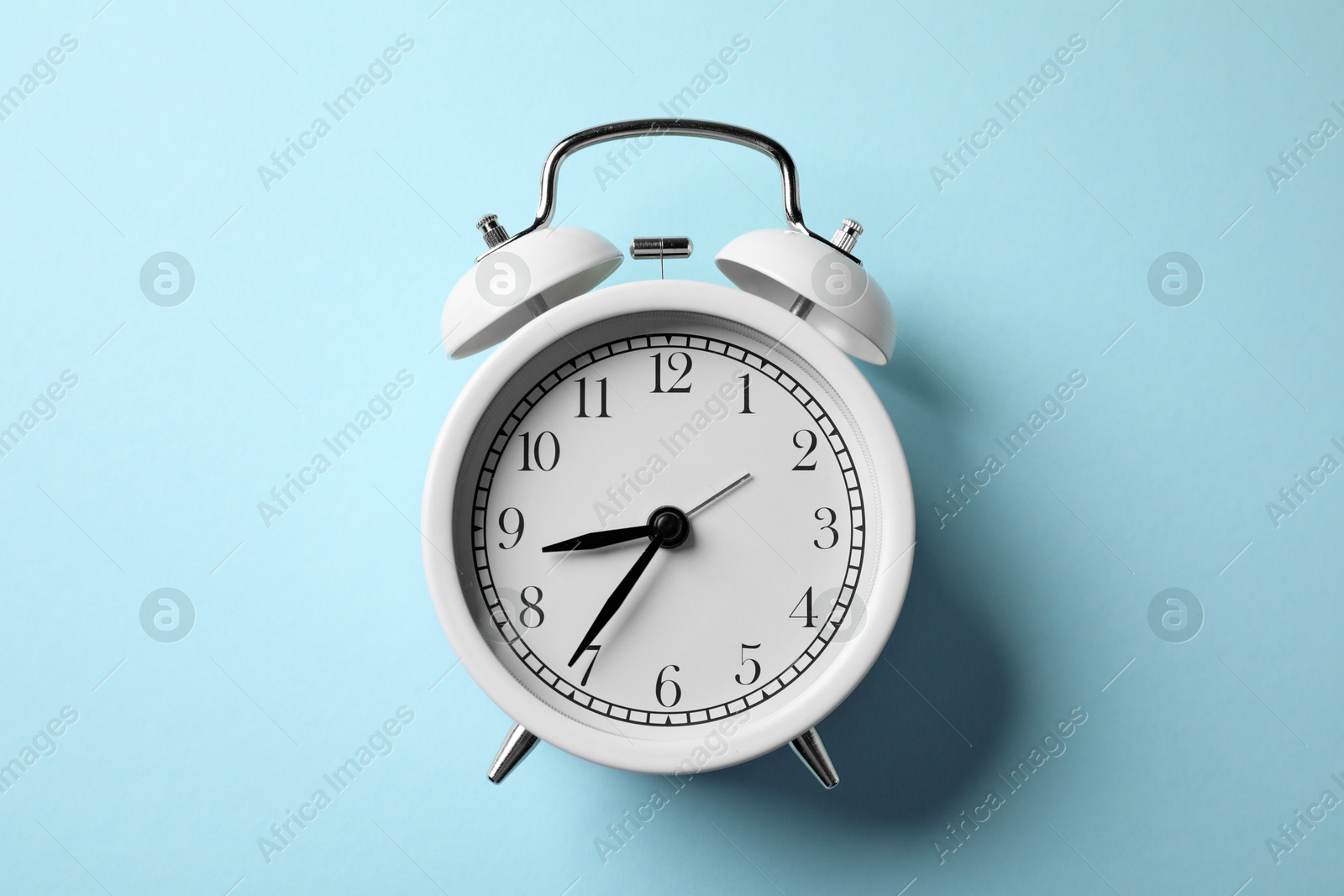White alarm clock on light blue background, top view Photo of White alarm clock on light blue background, top view