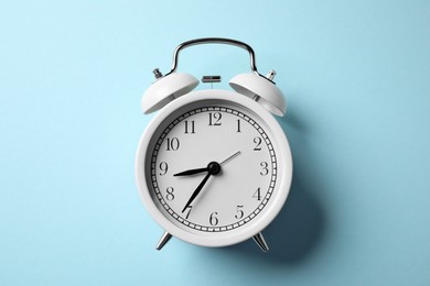Photo of White alarm clock on light blue background, top view