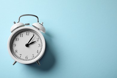 Photo of White alarm clock on light blue background, top view. Space for text