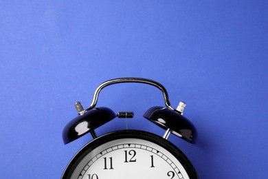 Photo of Black alarm clock on blue background, top view