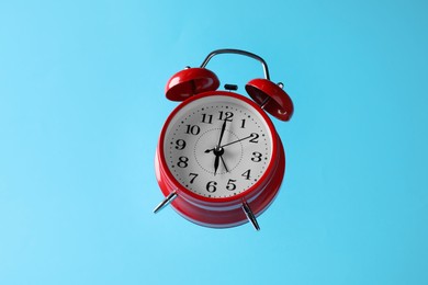 Photo of Red alarm clock in air on light blue background