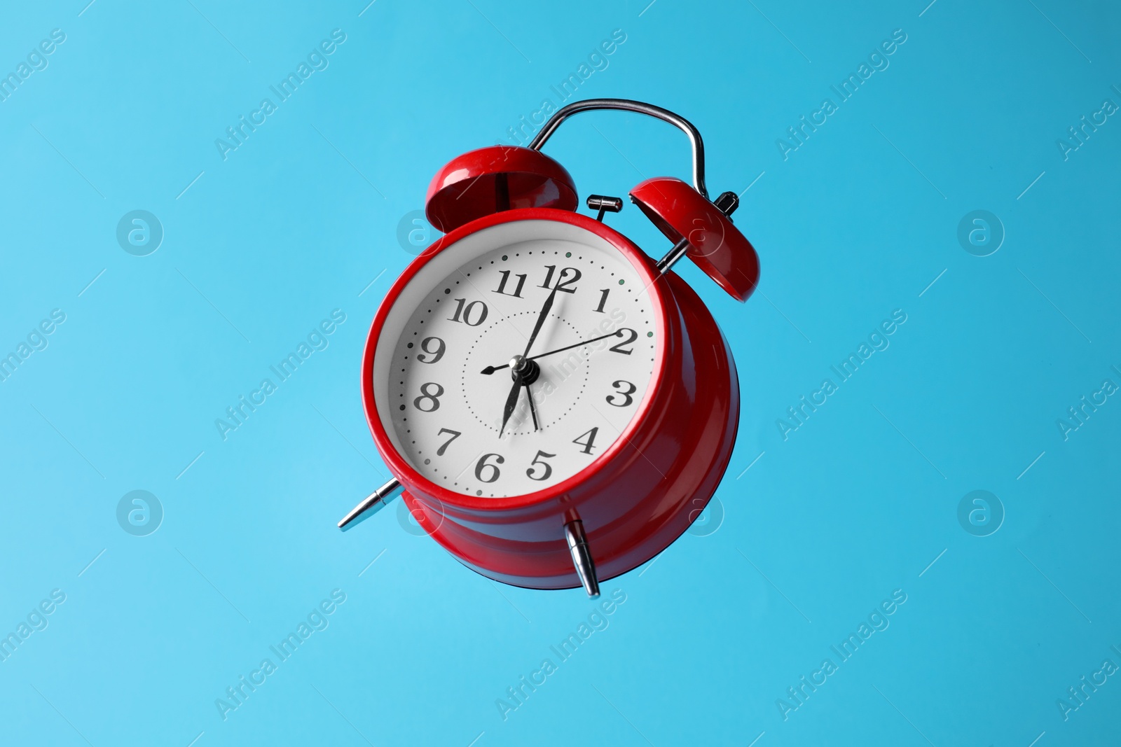 Red alarm clock in air on light blue background Photo of Red alarm clock in air on light blue background