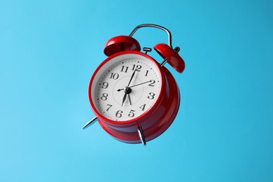Photo of Red alarm clock in air on light blue background