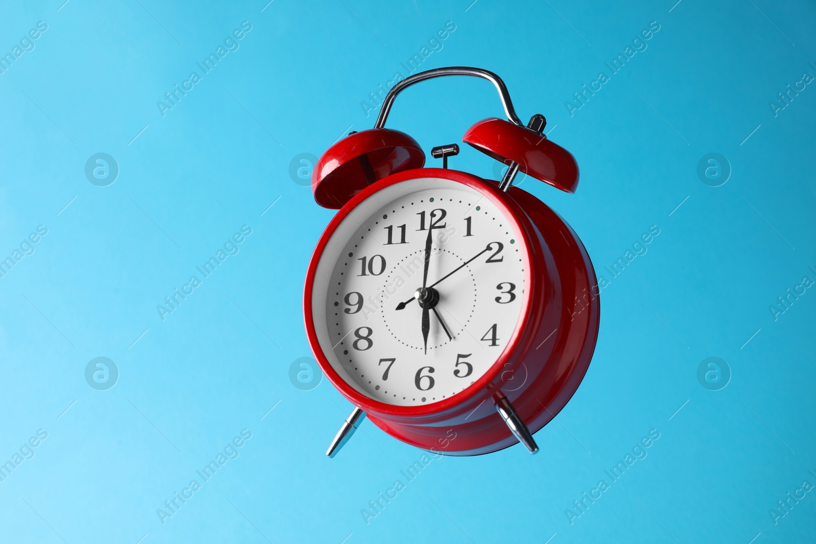 Red alarm clock in air on light blue background Photo of Red alarm clock in air on light blue background