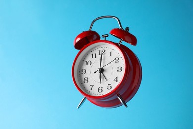 Photo of Red alarm clock in air on light blue background