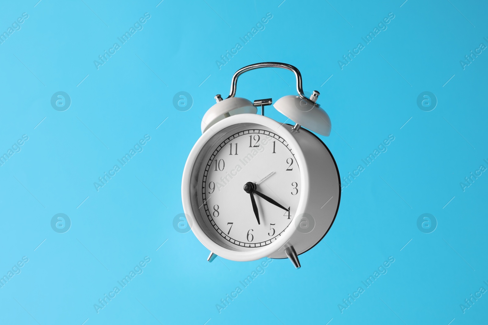 White alarm clock in air on light blue background Photo of White alarm clock in air on light blue background
