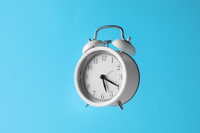 Photo of White alarm clock in air on light blue background