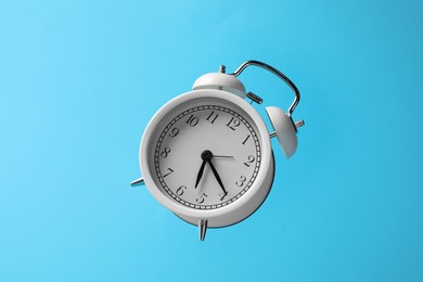 Photo of White alarm clock in air on light blue background