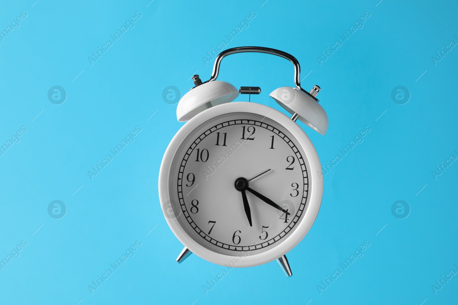 White alarm clock in air on light blue background Photo of White alarm clock in air on light blue background