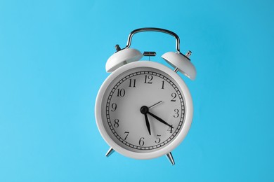 Photo of White alarm clock in air on light blue background
