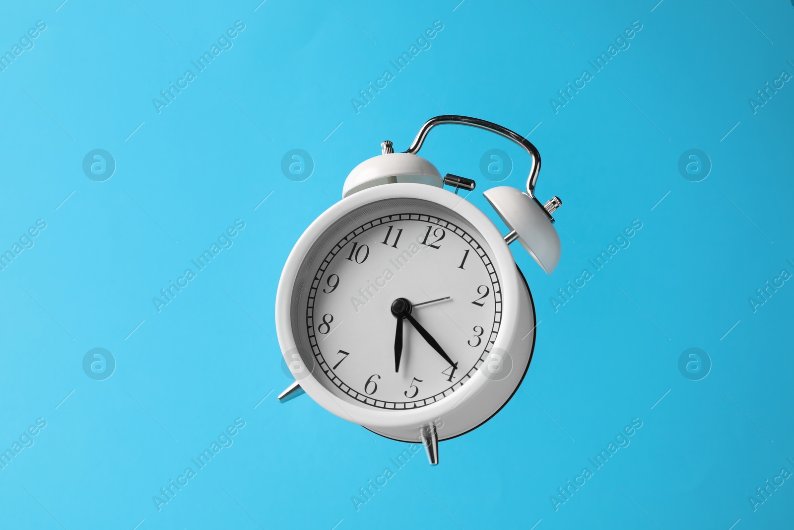 White alarm clock in air on light blue background Photo of White alarm clock in air on light blue background