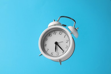 Photo of White alarm clock in air on light blue background