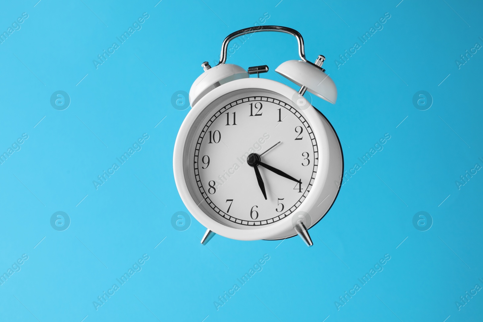 White alarm clock in air on light blue background Photo of White alarm clock in air on light blue background