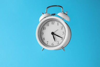 Photo of White alarm clock in air on light blue background