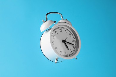Photo of White alarm clock in air on light blue background