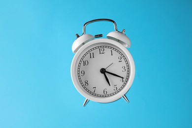 Photo of White alarm clock in air on light blue background