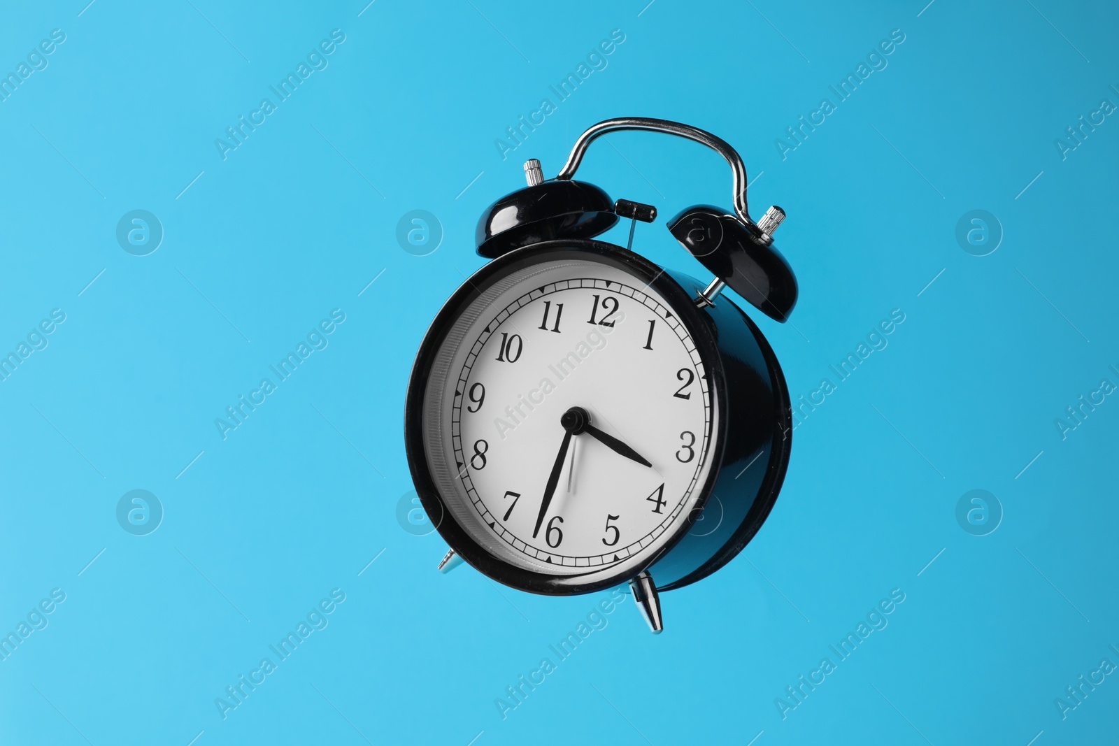Black alarm clock in air on light blue background Photo of Black alarm clock in air on light blue background