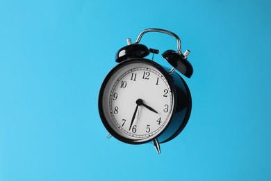 Photo of Black alarm clock in air on light blue background