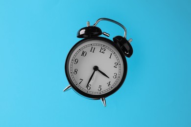 Photo of Black alarm clock in air on light blue background