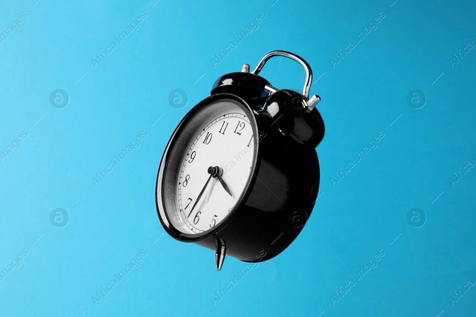 Photo of Black alarm clock in air on light blue background