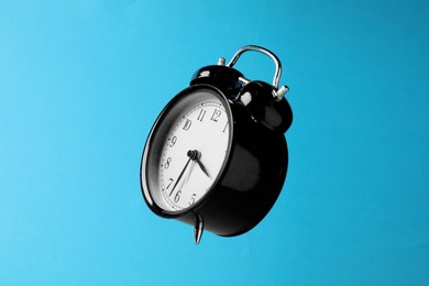Photo of Black alarm clock in air on light blue background