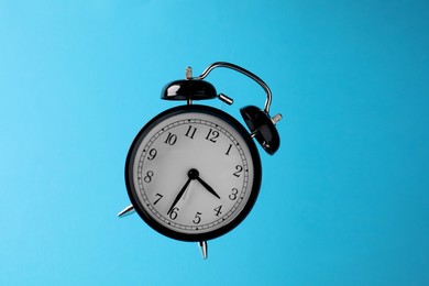 Photo of Black alarm clock in air on light blue background