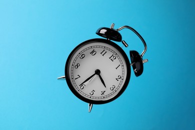 Photo of Black alarm clock in air on light blue background