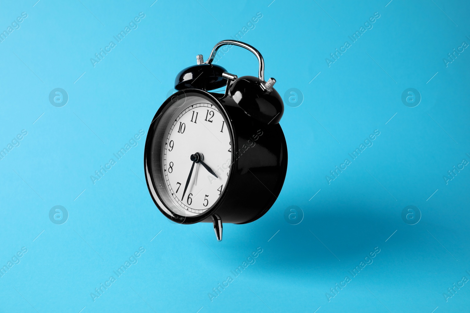 Photo of Black alarm clock in air on light blue background