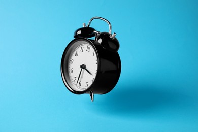 Photo of Black alarm clock in air on light blue background
