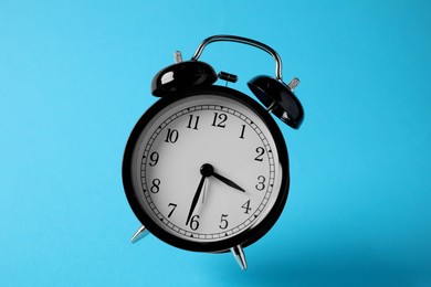 Photo of Black alarm clock in air on light blue background