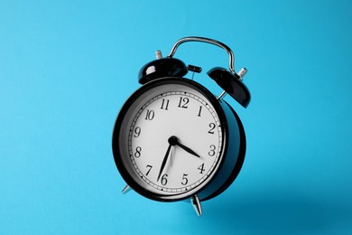 Photo of Black alarm clock in air on light blue background
