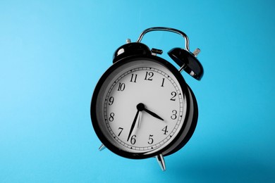 Photo of Black alarm clock in air on light blue background