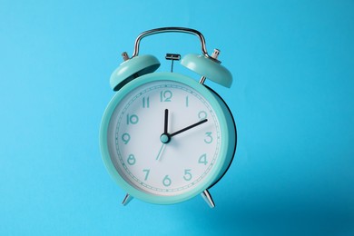 Photo of Turquoise alarm clock in air on light blue background