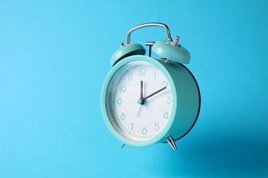 Photo of Turquoise alarm clock in air on light blue background
