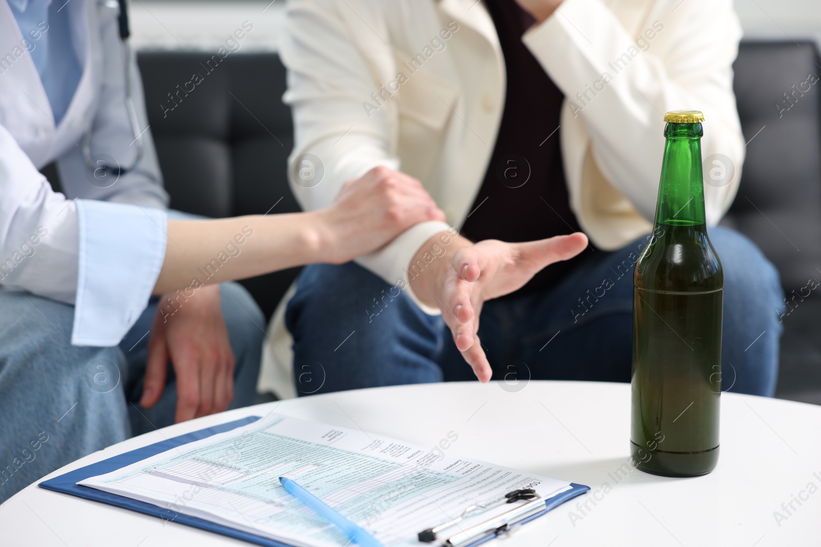 Photo of Alcoholic man having appointment with healthcare specialist in clinic, focus on bottle of beer. Addiction treatment