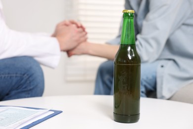 Photo of Dependent woman having appointment with addiction specialist in clinic, focus on bottle of beer