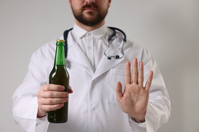 Photo of Healthcare specialist with bottle of beer showing stop gesture on light background, closeup. Addiction treatment