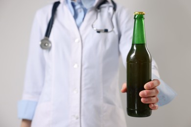 Photo of Healthcare specialist with bottle of beer on light background, closeup. Addiction treatment