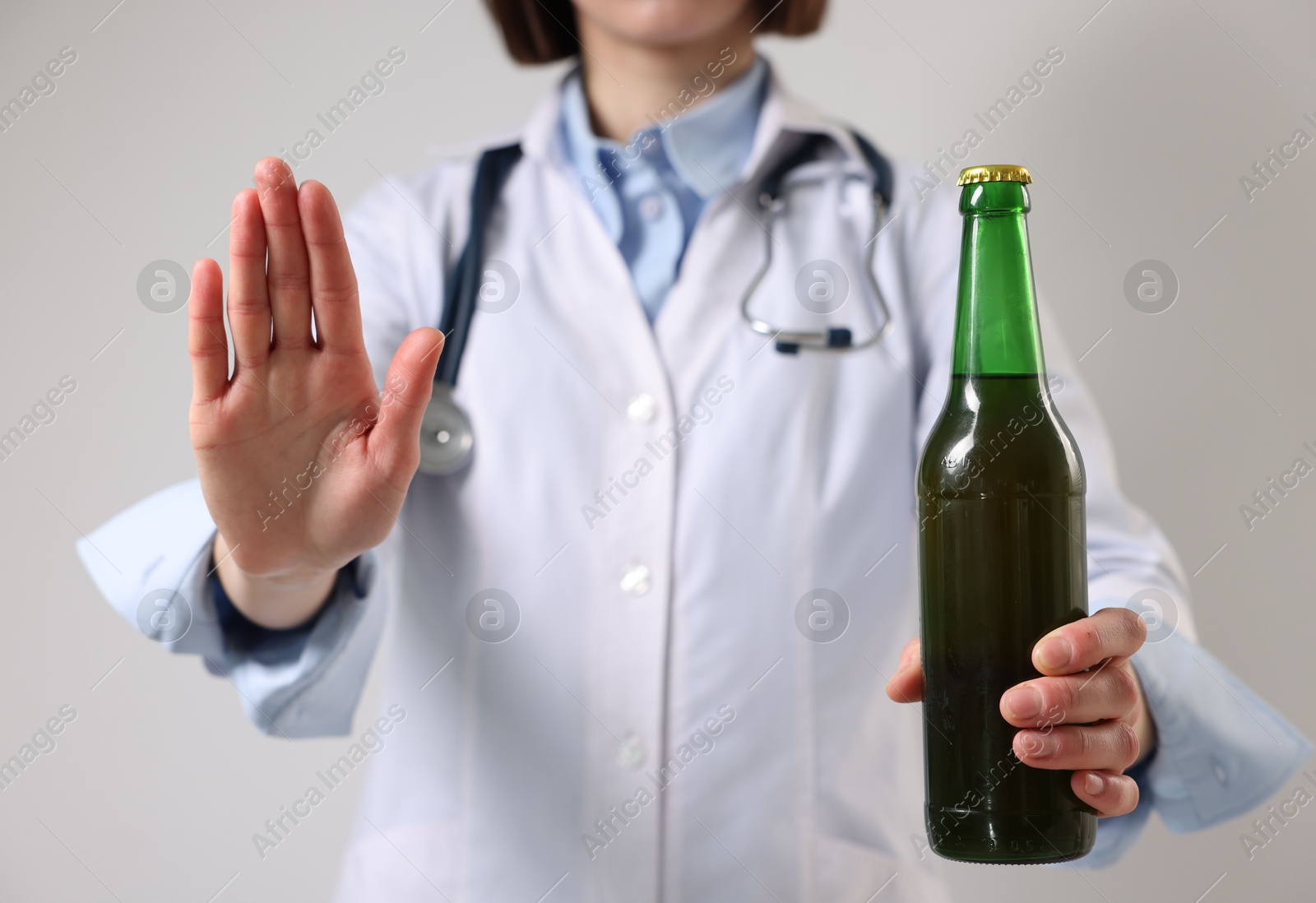 Photo of Healthcare specialist with bottle of beer showing stop gesture on light background, closeup. Addiction treatment