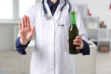 Photo of Healthcare specialist with bottle of beer showing stop gesture in clinic, closeup. Addiction treatment