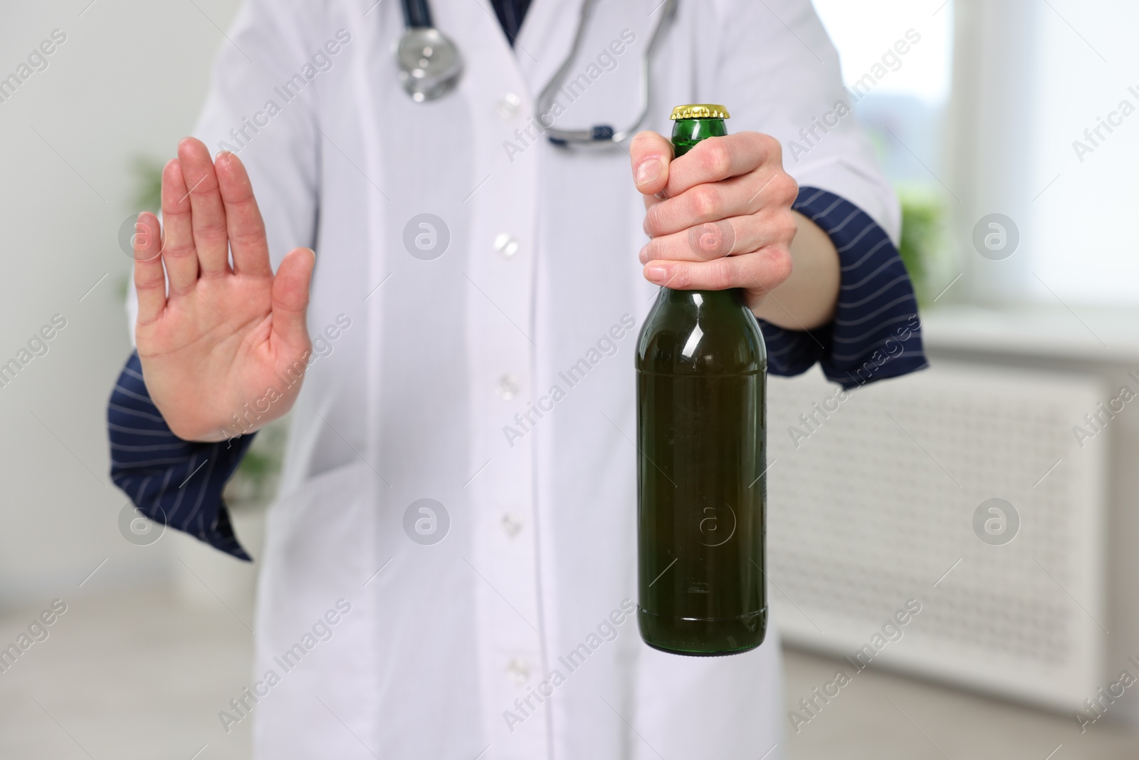 Photo of Healthcare specialist with bottle of beer showing stop gesture in clinic, closeup. Addiction treatment