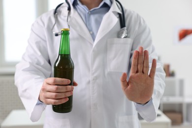 Photo of Healthcare specialist with bottle of beer showing stop gesture in clinic, closeup. Addiction treatment