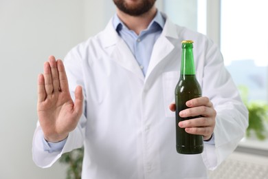 Photo of Healthcare specialist with bottle of beer showing stop gesture in clinic, closeup. Addiction treatment