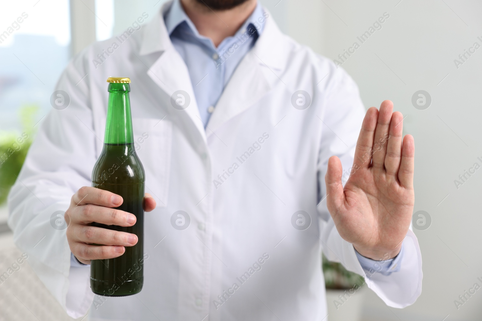 Photo of Healthcare specialist with bottle of beer showing stop gesture in clinic, closeup. Addiction treatment