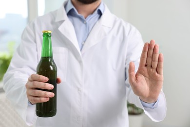 Photo of Healthcare specialist with bottle of beer showing stop gesture in clinic, closeup. Addiction treatment