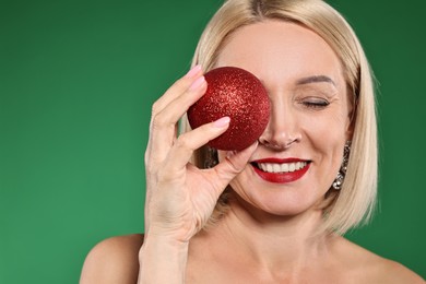 Photo of Smiling woman with perfect makeup and Christmas bauble on green background. Space for text