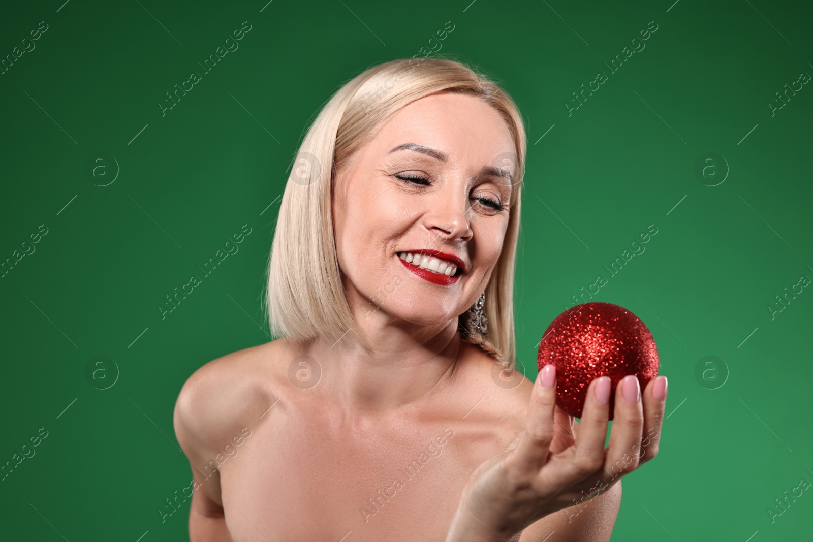 Photo of Smiling woman with perfect makeup and Christmas bauble on green background