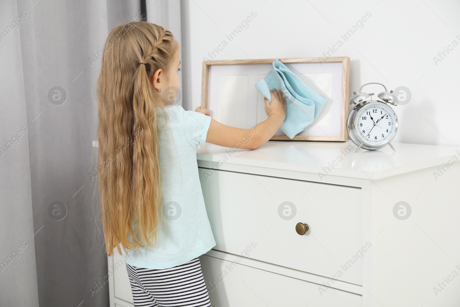 Photo of Little helper. Cute girl wiping dust from frame at home