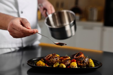 Photo of Professional chef adding sauce to delicious dish at table indoors, closeup