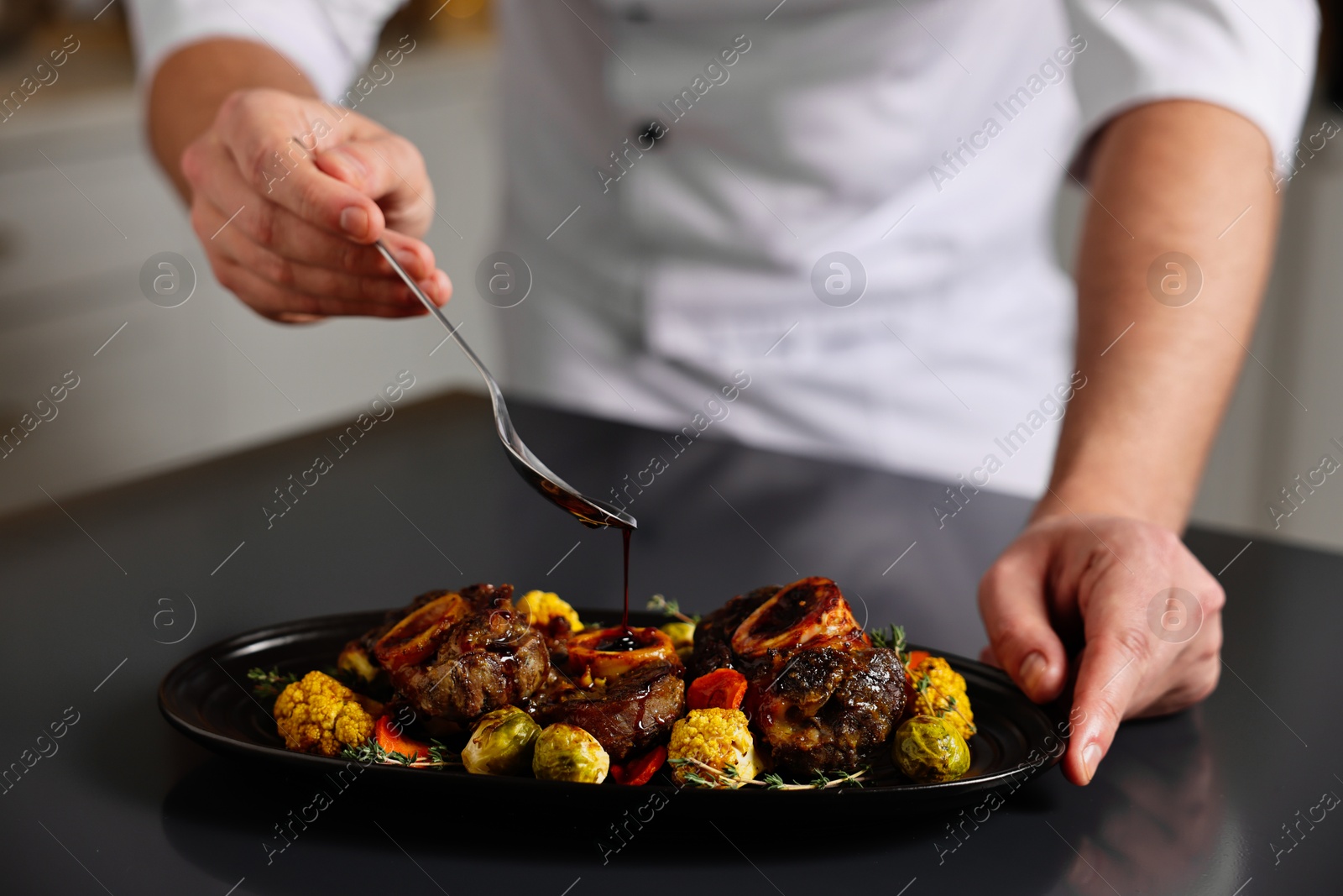 Photo of Professional chef adding sauce to delicious dish at table indoors, closeup